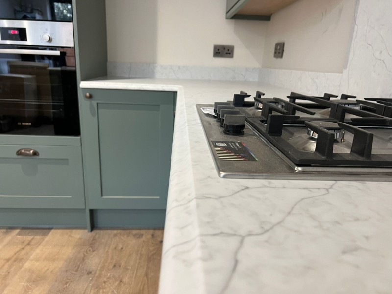 Green kitchen with white & grey veined worktop, close up shot of the edge of the worktop